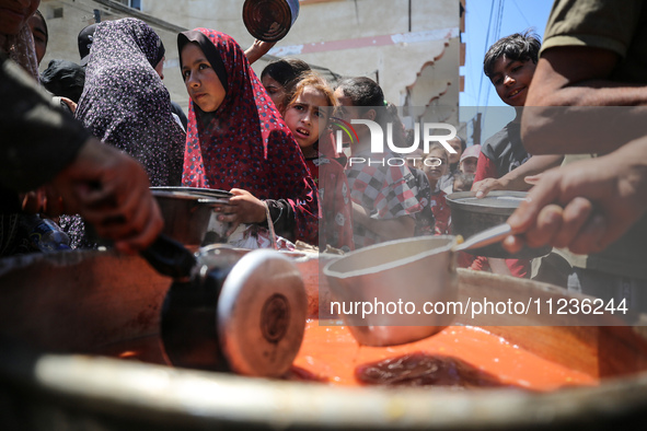 Displaced Palestinians are receiving food portions from a large pot at a public kitchen in Deir el-Balah in the central Gaza Strip on May 13...