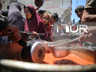 Displaced Palestinians are receiving food portions from a large pot at a public kitchen in Deir el-Balah in the central Gaza Strip on May 13...