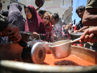 Displaced Palestinians are receiving food portions from a large pot at a public kitchen in Deir el-Balah in the central Gaza Strip on May 13...