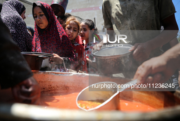 Displaced Palestinians are receiving food portions from a large pot at a public kitchen in Deir el-Balah in the central Gaza Strip on May 13...