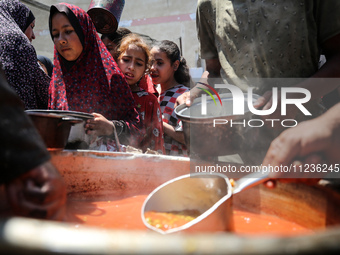 Displaced Palestinians are receiving food portions from a large pot at a public kitchen in Deir el-Balah in the central Gaza Strip on May 13...