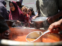 Displaced Palestinians are receiving food portions from a large pot at a public kitchen in Deir el-Balah in the central Gaza Strip on May 13...