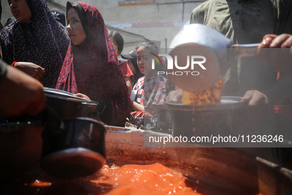 Displaced Palestinians are receiving food portions from a large pot at a public kitchen in Deir el-Balah in the central Gaza Strip on May 13...