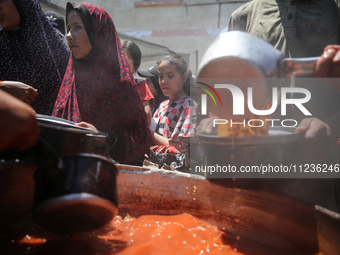 Displaced Palestinians are receiving food portions from a large pot at a public kitchen in Deir el-Balah in the central Gaza Strip on May 13...