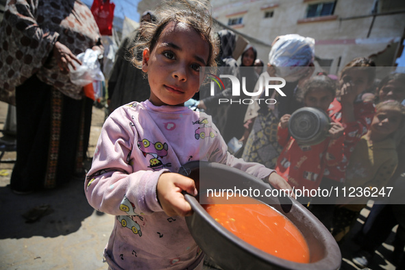 Displaced Palestinians are receiving food portions from a large pot at a public kitchen in Deir el-Balah in the central Gaza Strip on May 13...