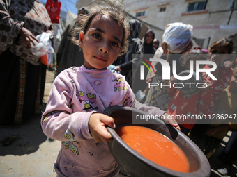 Displaced Palestinians are receiving food portions from a large pot at a public kitchen in Deir el-Balah in the central Gaza Strip on May 13...