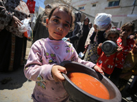 Displaced Palestinians are receiving food portions from a large pot at a public kitchen in Deir el-Balah in the central Gaza Strip on May 13...