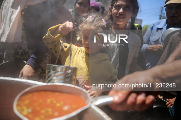 Displaced Palestinians are receiving food portions from a large pot at a public kitchen in Deir el-Balah in the central Gaza Strip on May 13...