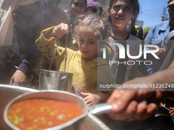 Displaced Palestinians are receiving food portions from a large pot at a public kitchen in Deir el-Balah in the central Gaza Strip on May 13...