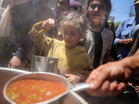 Displaced Palestinians are receiving food portions from a large pot at a public kitchen in Deir el-Balah in the central Gaza Strip on May 13...