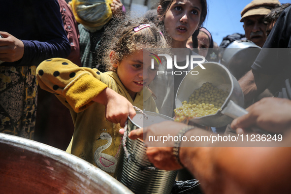 Displaced Palestinians are receiving food portions from a large pot at a public kitchen in Deir el-Balah in the central Gaza Strip on May 13...