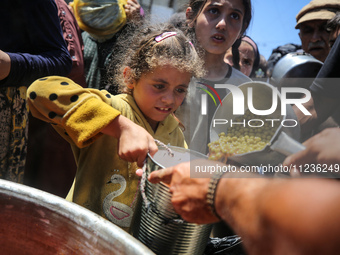 Displaced Palestinians are receiving food portions from a large pot at a public kitchen in Deir el-Balah in the central Gaza Strip on May 13...