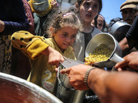 Displaced Palestinians are receiving food portions from a large pot at a public kitchen in Deir el-Balah in the central Gaza Strip on May 13...