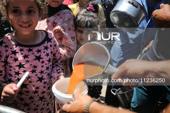 Displaced Palestinians are receiving food portions from a large pot at a public kitchen in Deir el-Balah in the central Gaza Strip on May 13...