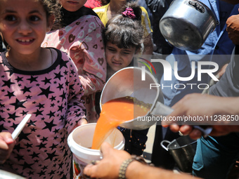 Displaced Palestinians are receiving food portions from a large pot at a public kitchen in Deir el-Balah in the central Gaza Strip on May 13...