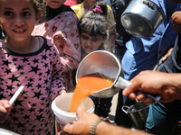 Displaced Palestinians are receiving food portions from a large pot at a public kitchen in Deir el-Balah in the central Gaza Strip on May 13...