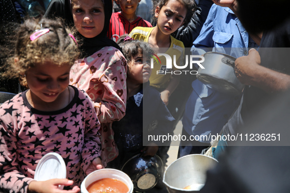 Displaced Palestinians are receiving food portions from a large pot at a public kitchen in Deir el-Balah in the central Gaza Strip on May 13...