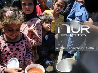 Displaced Palestinians are receiving food portions from a large pot at a public kitchen in Deir el-Balah in the central Gaza Strip on May 13...