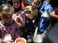 Displaced Palestinians are receiving food portions from a large pot at a public kitchen in Deir el-Balah in the central Gaza Strip on May 13...