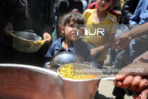 Displaced Palestinians are receiving food portions from a large pot at a public kitchen in Deir el-Balah in the central Gaza Strip on May 13...