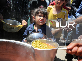 Displaced Palestinians are receiving food portions from a large pot at a public kitchen in Deir el-Balah in the central Gaza Strip on May 13...