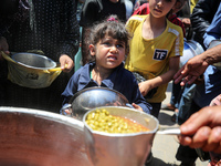 Displaced Palestinians are receiving food portions from a large pot at a public kitchen in Deir el-Balah in the central Gaza Strip on May 13...