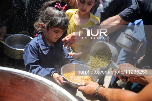 Displaced Palestinians are receiving food portions from a large pot at a public kitchen in Deir el-Balah in the central Gaza Strip on May 13...