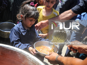 Displaced Palestinians are receiving food portions from a large pot at a public kitchen in Deir el-Balah in the central Gaza Strip on May 13...