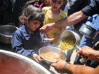 Displaced Palestinians are receiving food portions from a large pot at a public kitchen in Deir el-Balah in the central Gaza Strip on May 13...