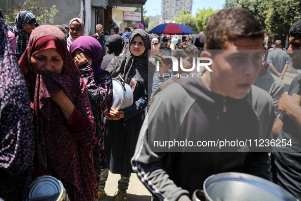 Displaced Palestinians are queuing to receive food rations from a public kitchen in Deir el-Balah in the central Gaza Strip on May 13, 2024,...