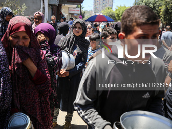 Displaced Palestinians are queuing to receive food rations from a public kitchen in Deir el-Balah in the central Gaza Strip on May 13, 2024,...