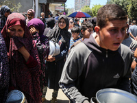 Displaced Palestinians are queuing to receive food rations from a public kitchen in Deir el-Balah in the central Gaza Strip on May 13, 2024,...