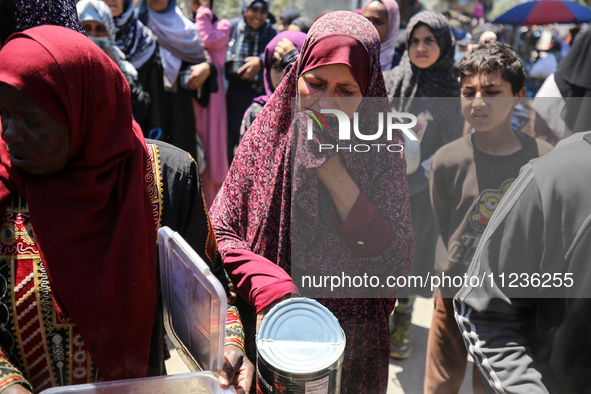 Displaced Palestinians are queuing to receive food rations from a public kitchen in Deir el-Balah in the central Gaza Strip on May 13, 2024,...