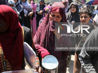 Displaced Palestinians are queuing to receive food rations from a public kitchen in Deir el-Balah in the central Gaza Strip on May 13, 2024,...