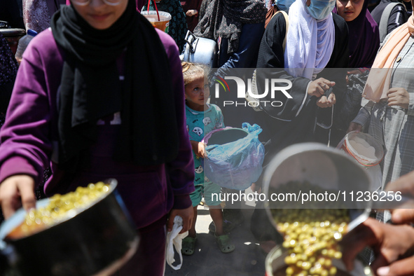 Displaced Palestinians are receiving food portions from a large pot at a public kitchen in Deir el-Balah in the central Gaza Strip on May 13...