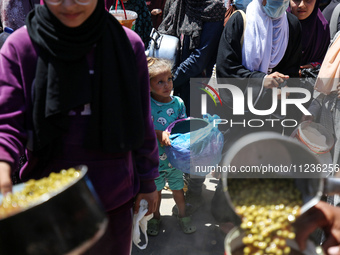 Displaced Palestinians are receiving food portions from a large pot at a public kitchen in Deir el-Balah in the central Gaza Strip on May 13...