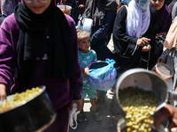 Displaced Palestinians are receiving food portions from a large pot at a public kitchen in Deir el-Balah in the central Gaza Strip on May 13...