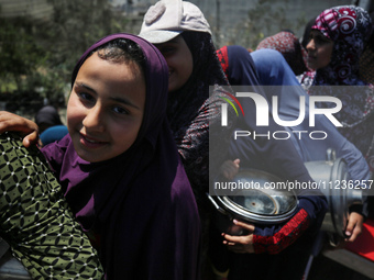 Displaced Palestinians are queuing to receive food rations from a public kitchen in Deir el-Balah in the central Gaza Strip on May 13, 2024,...