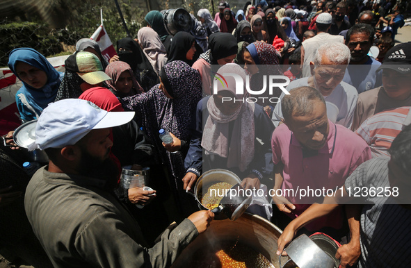 Displaced Palestinians are receiving food portions from a large pot at a public kitchen in Deir el-Balah in the central Gaza Strip on May 13...