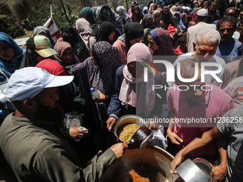 Displaced Palestinians are receiving food portions from a large pot at a public kitchen in Deir el-Balah in the central Gaza Strip on May 13...