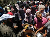 Displaced Palestinians are receiving food portions from a large pot at a public kitchen in Deir el-Balah in the central Gaza Strip on May 13...