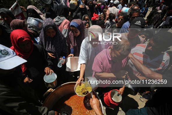 Displaced Palestinians are receiving food portions from a large pot at a public kitchen in Deir el-Balah in the central Gaza Strip on May 13...