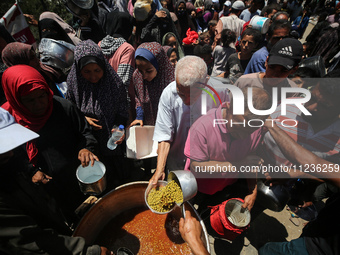 Displaced Palestinians are receiving food portions from a large pot at a public kitchen in Deir el-Balah in the central Gaza Strip on May 13...