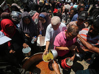 Displaced Palestinians are receiving food portions from a large pot at a public kitchen in Deir el-Balah in the central Gaza Strip on May 13...