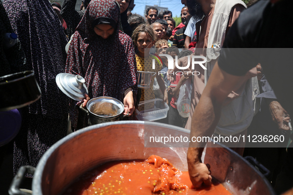 Displaced Palestinians are receiving food portions from a large pot at a public kitchen in Deir el-Balah in the central Gaza Strip on May 13...