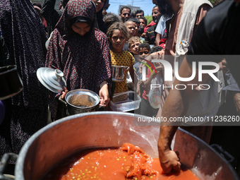 Displaced Palestinians are receiving food portions from a large pot at a public kitchen in Deir el-Balah in the central Gaza Strip on May 13...