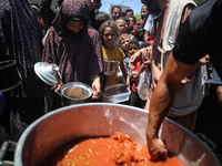 Displaced Palestinians are receiving food portions from a large pot at a public kitchen in Deir el-Balah in the central Gaza Strip on May 13...