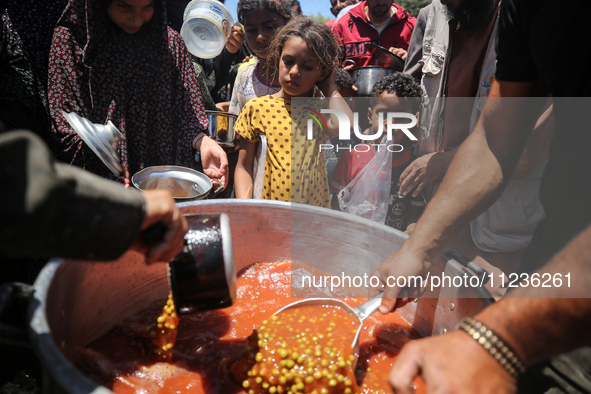 Displaced Palestinians are receiving food portions from a large pot at a public kitchen in Deir el-Balah in the central Gaza Strip on May 13...