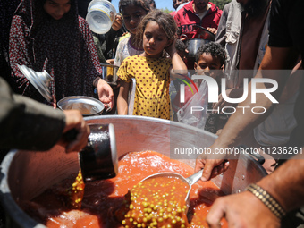 Displaced Palestinians are receiving food portions from a large pot at a public kitchen in Deir el-Balah in the central Gaza Strip on May 13...