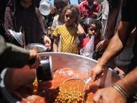 Displaced Palestinians are receiving food portions from a large pot at a public kitchen in Deir el-Balah in the central Gaza Strip on May 13...